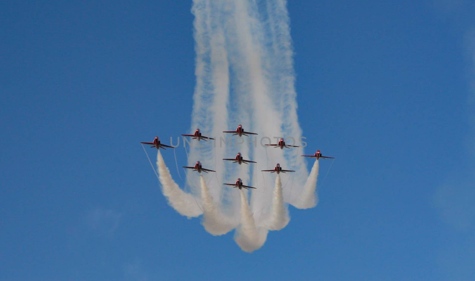 Royal air force red arrows in part of an air display flying in formation with white smoke trails in England.