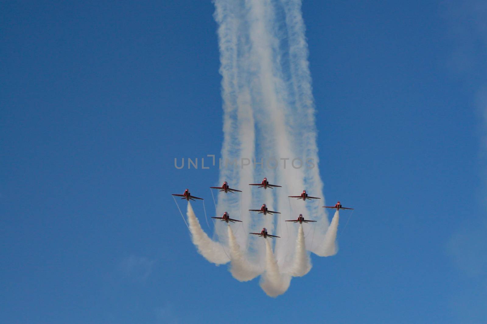 Royal air force red arrows in part of an air display flying in formation with white smoke trails in England.