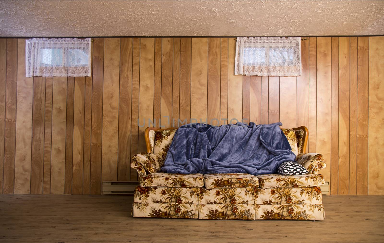 old couch from the 70s, in a basement, with a blue blanket