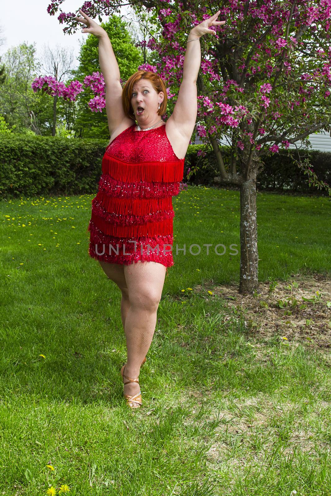 woman in her forties, wearing a sparkly dress, under a tree, doing a lady styling pose, doing a funny face