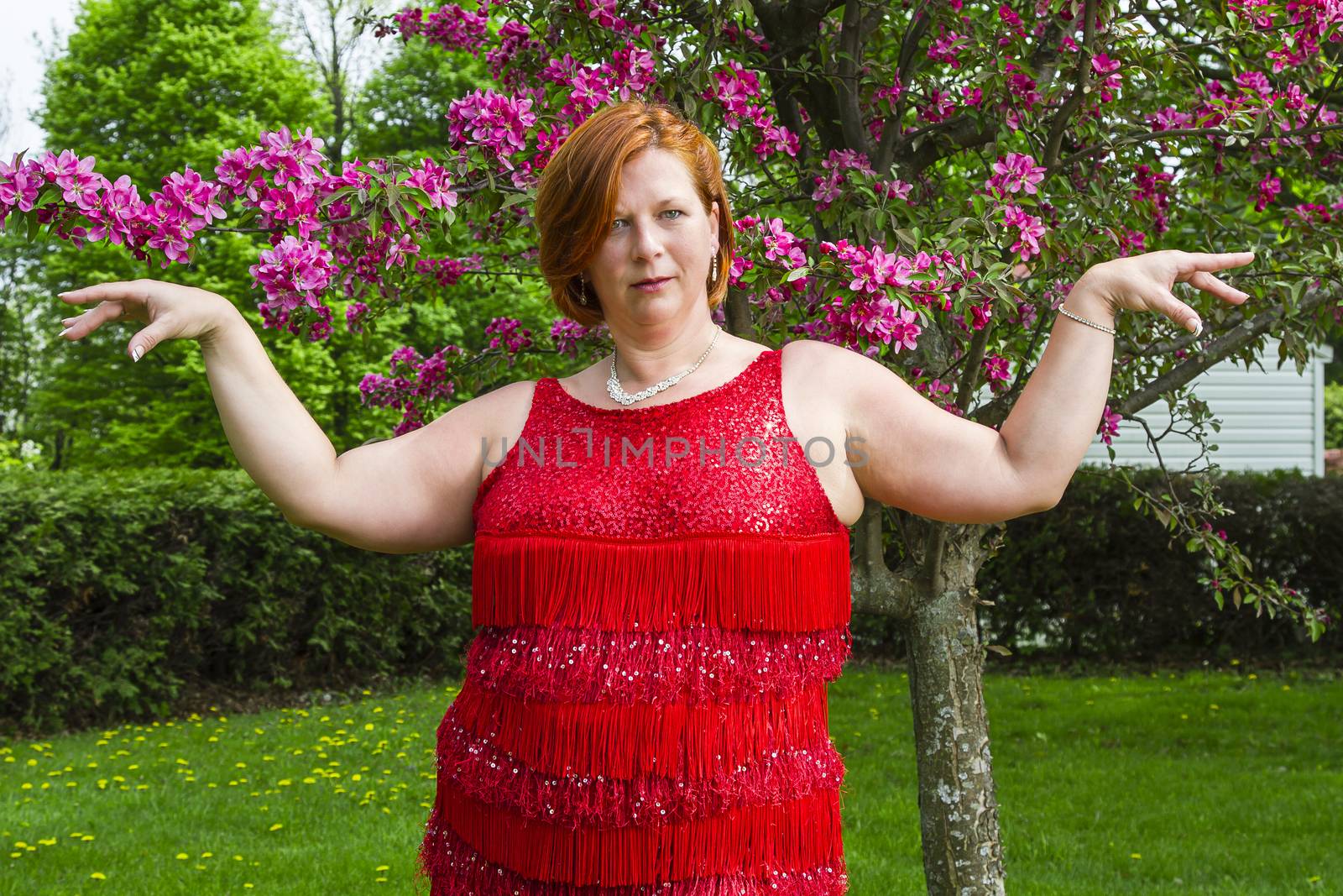 forty something red haired woman, wearing a sparkly dress, in front of a cherry tree, doing a ladystyling pose