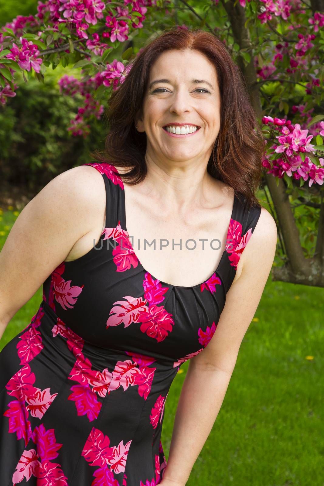 forty something brunette woman, wearing a summer dress, in front of a cherry tree