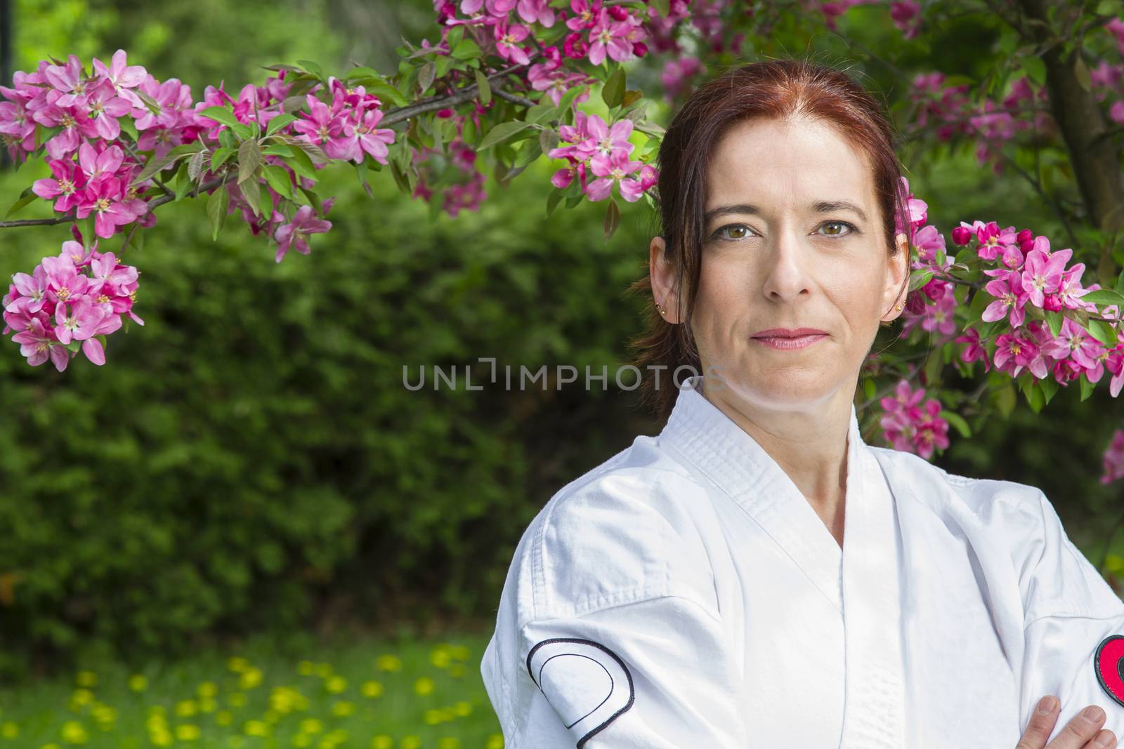forty something brunette woman, wearing a wearing karate gi, standing under a cherry tree