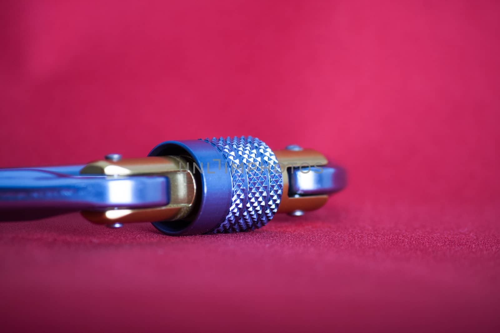 Angle close-up on a locking mechanism of an alluminium climbing carabiner on red background