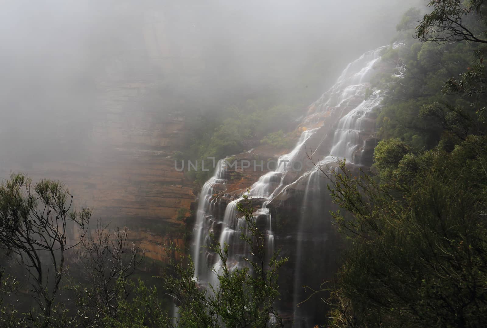 Waterfall flowing down the cliff face  with a heavy dense fog subduing visibility
