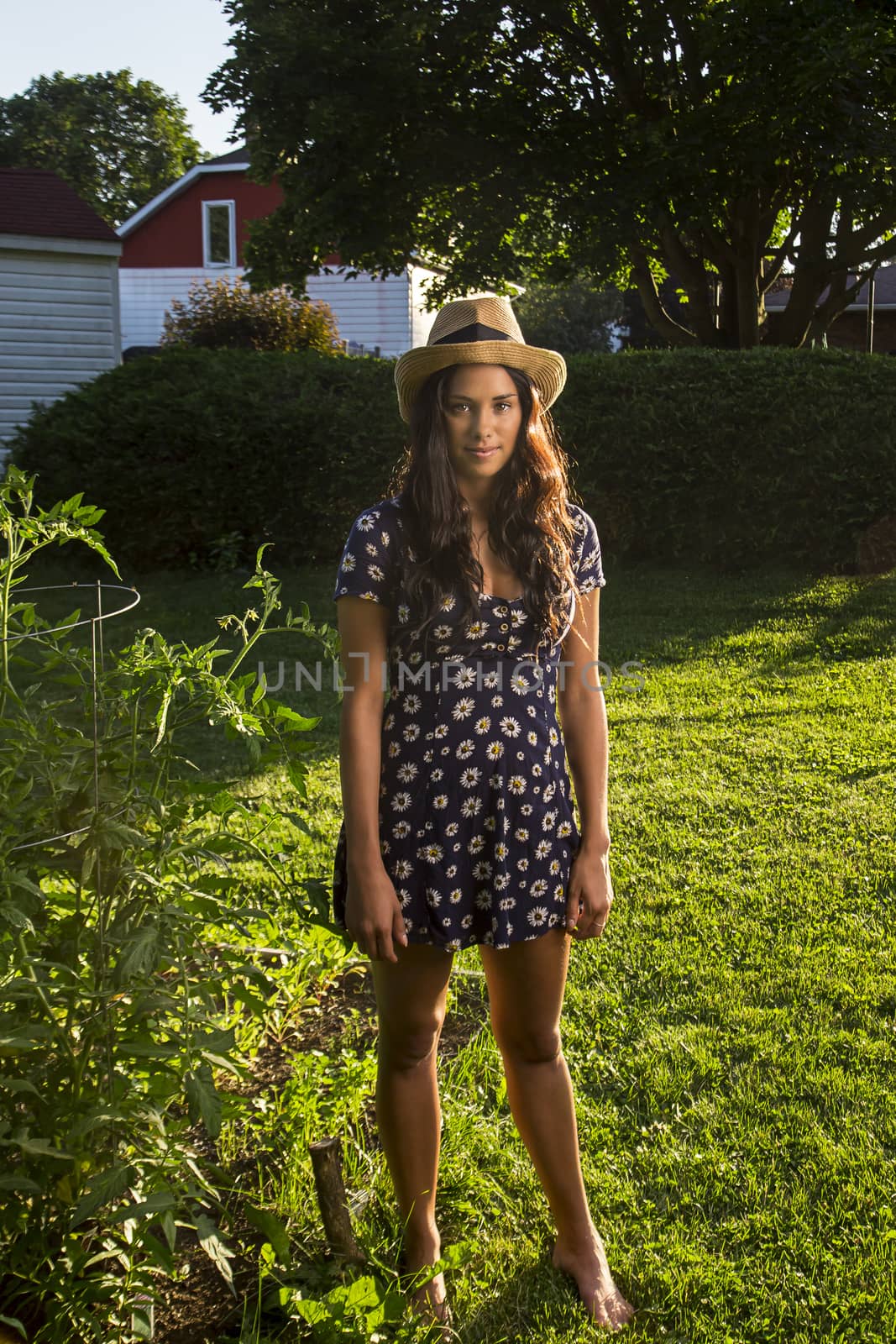 twenty something woman standing outside in the sun, wearing a sun dress and a straw hat