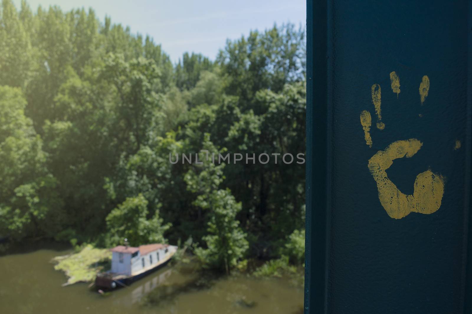 A yellow human handprint on steel bridge above boat on the green river