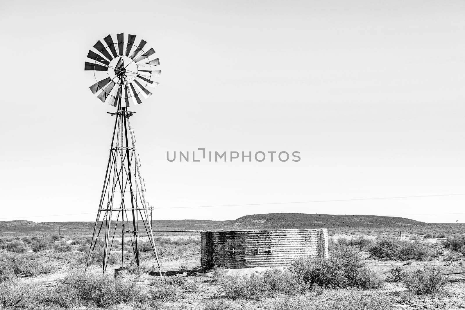 A typical rural Karoo scene in South Africa - a water pumping windmill with a leaking dam. Monochrome