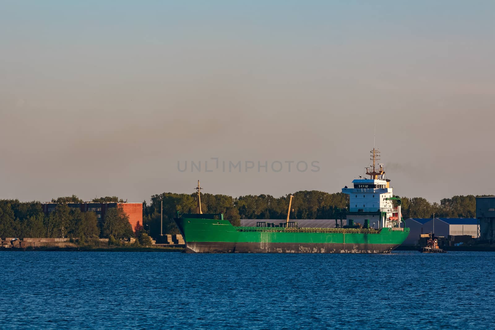 Green cargo ship leaves the port in a clear day