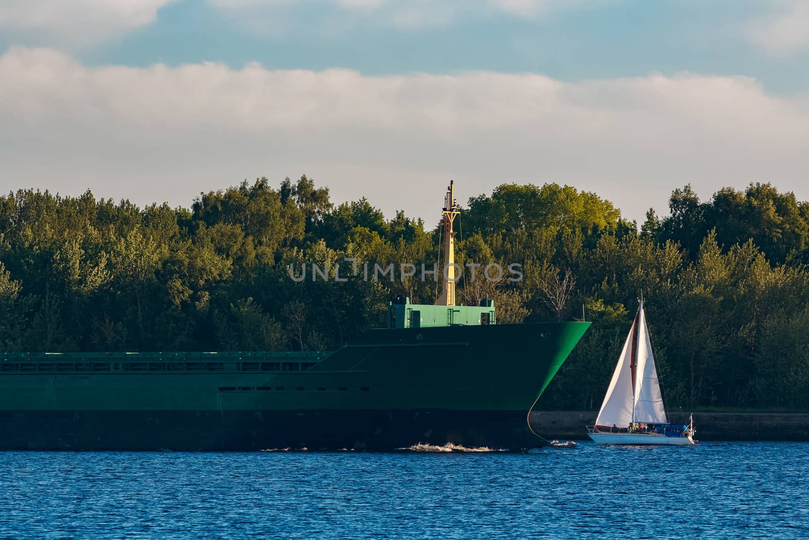 Green cargo ship leaves the port in a clear day