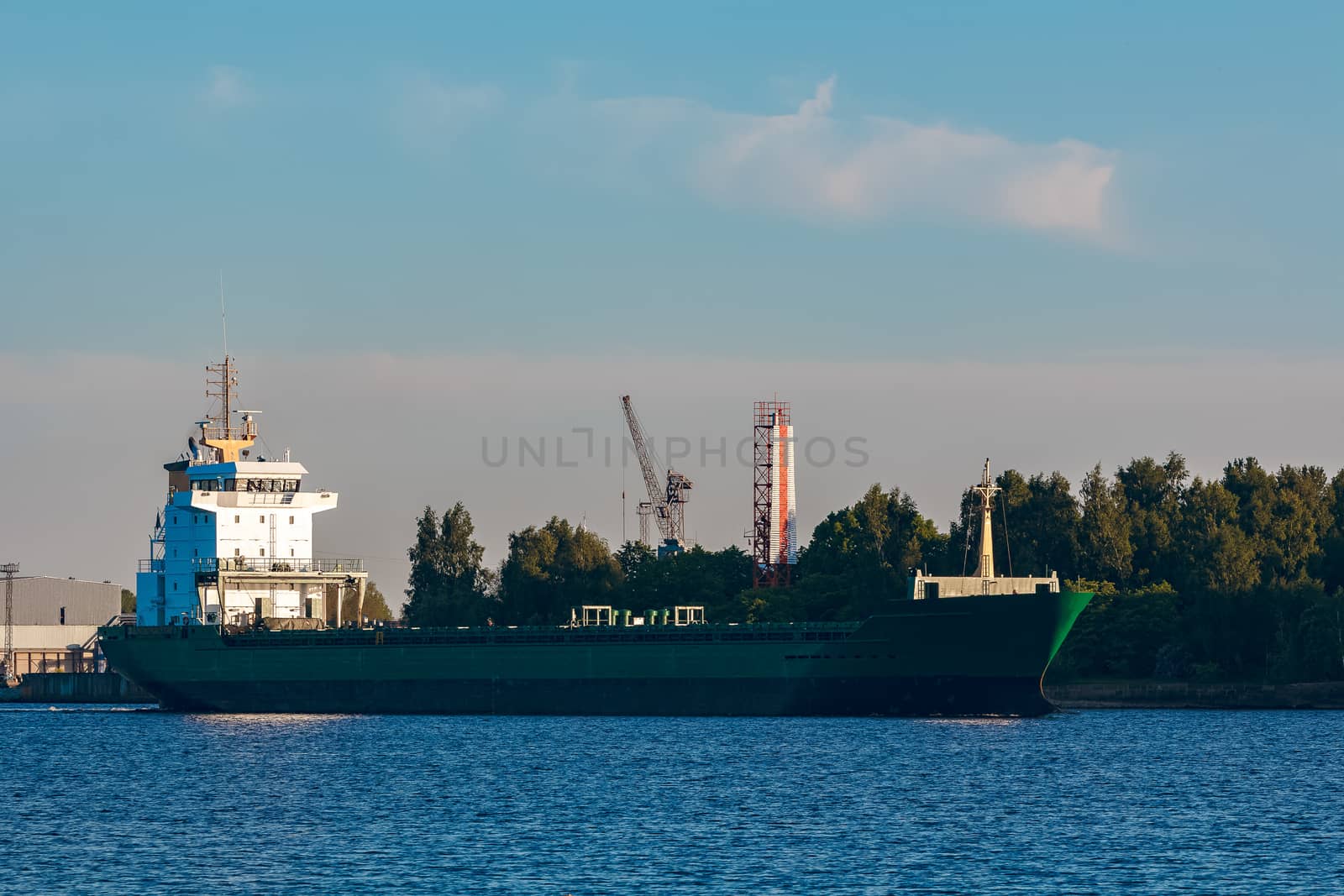 Green cargo ship leaves the port in a clear day