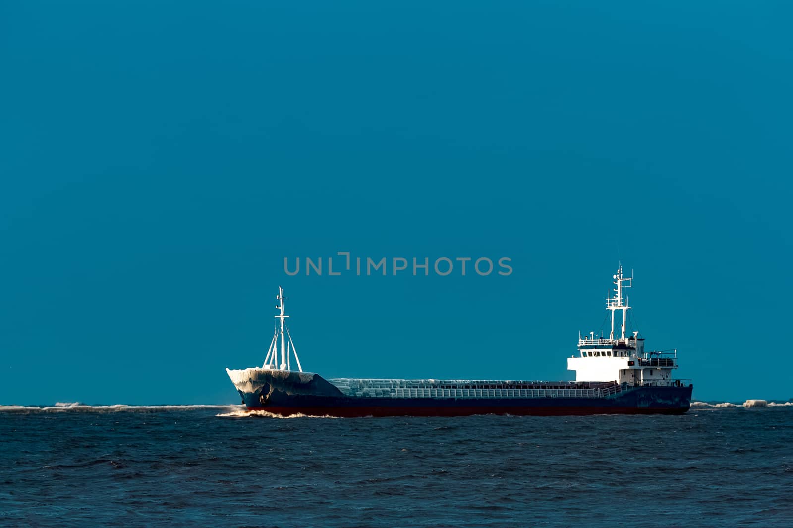 Blue bulk carrier moving from the sea in cold winter