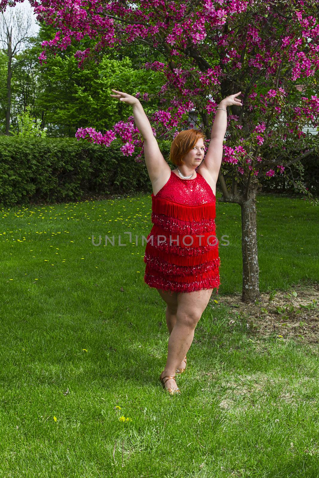 overweight forty year old woman in the middle of a lady styling dance pose, outside under a cherry tree