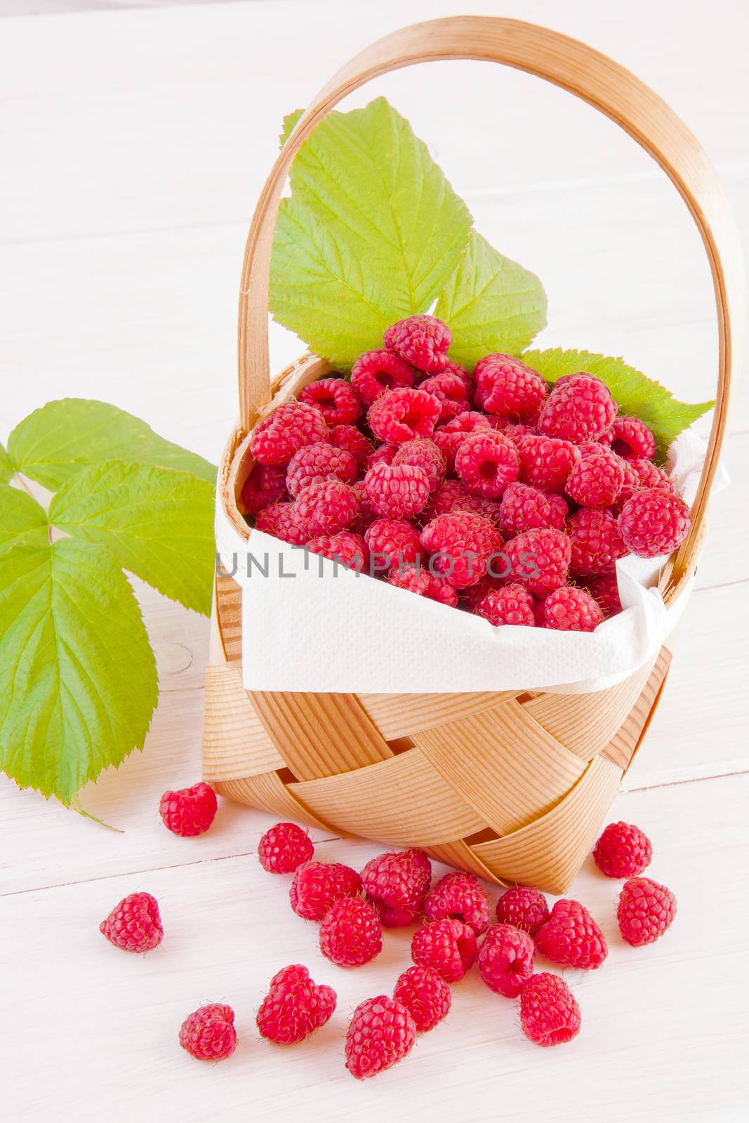Fresh fruits raspberries in a wooden little basket on a white table