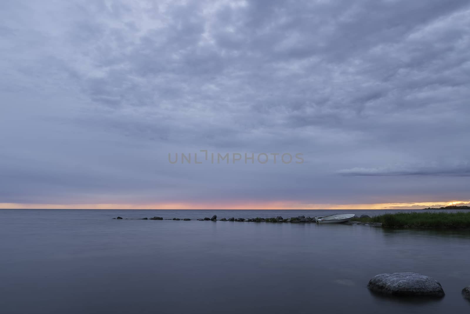 Rowboat by Ocean at Sunset with a partly cloudy sky.