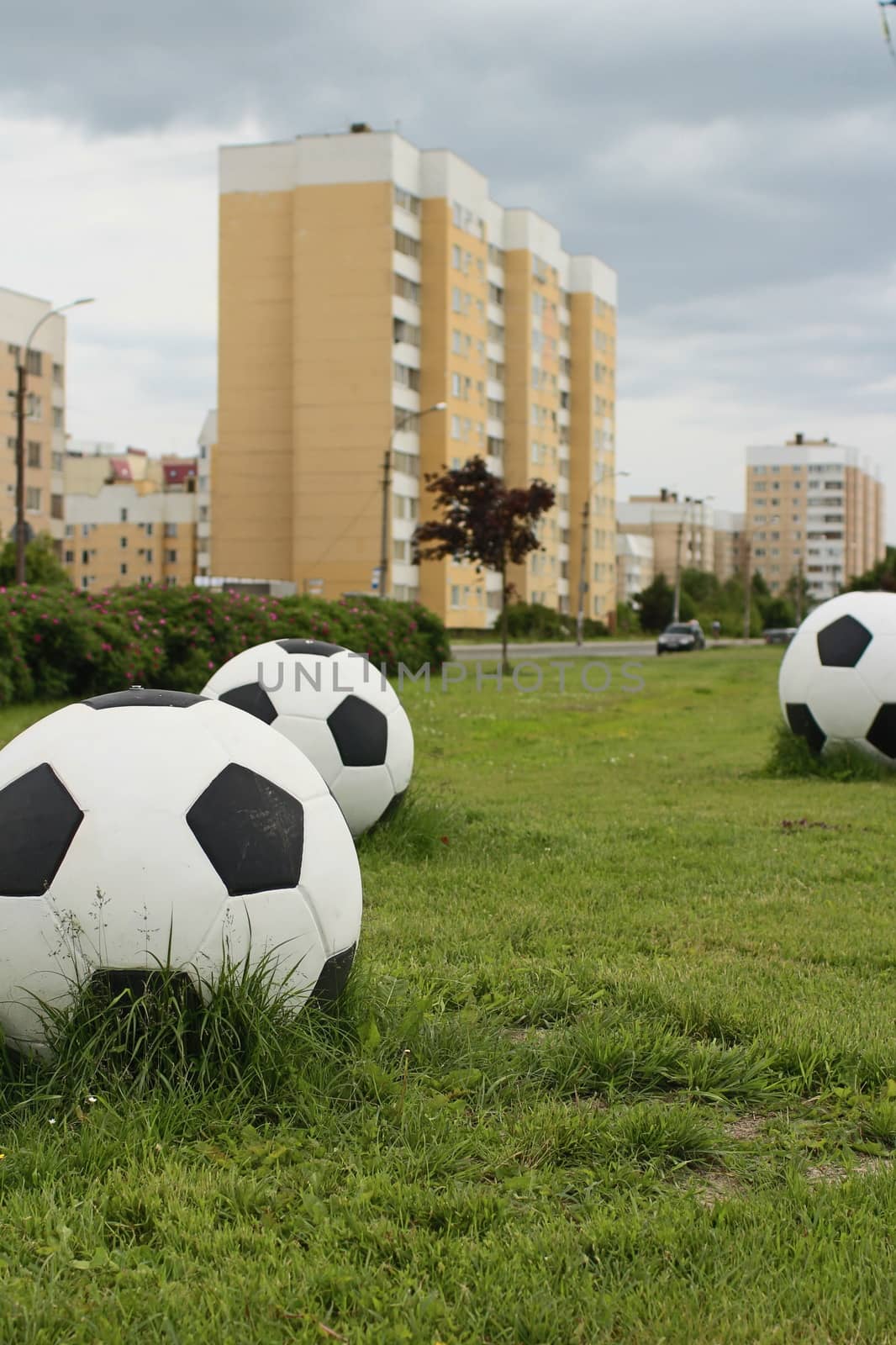 three big soccer balls on the green lawn cityscape