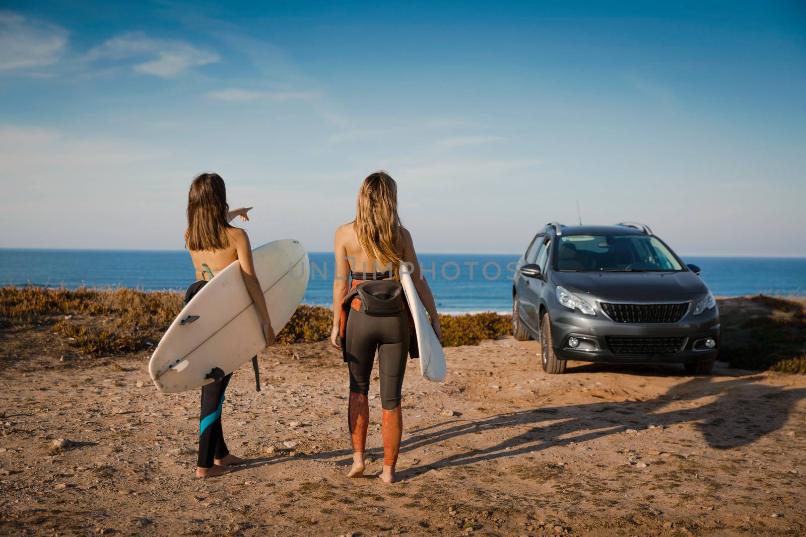 Two beautiful surfer girls near the coastline with her car, and getting ready for surfing