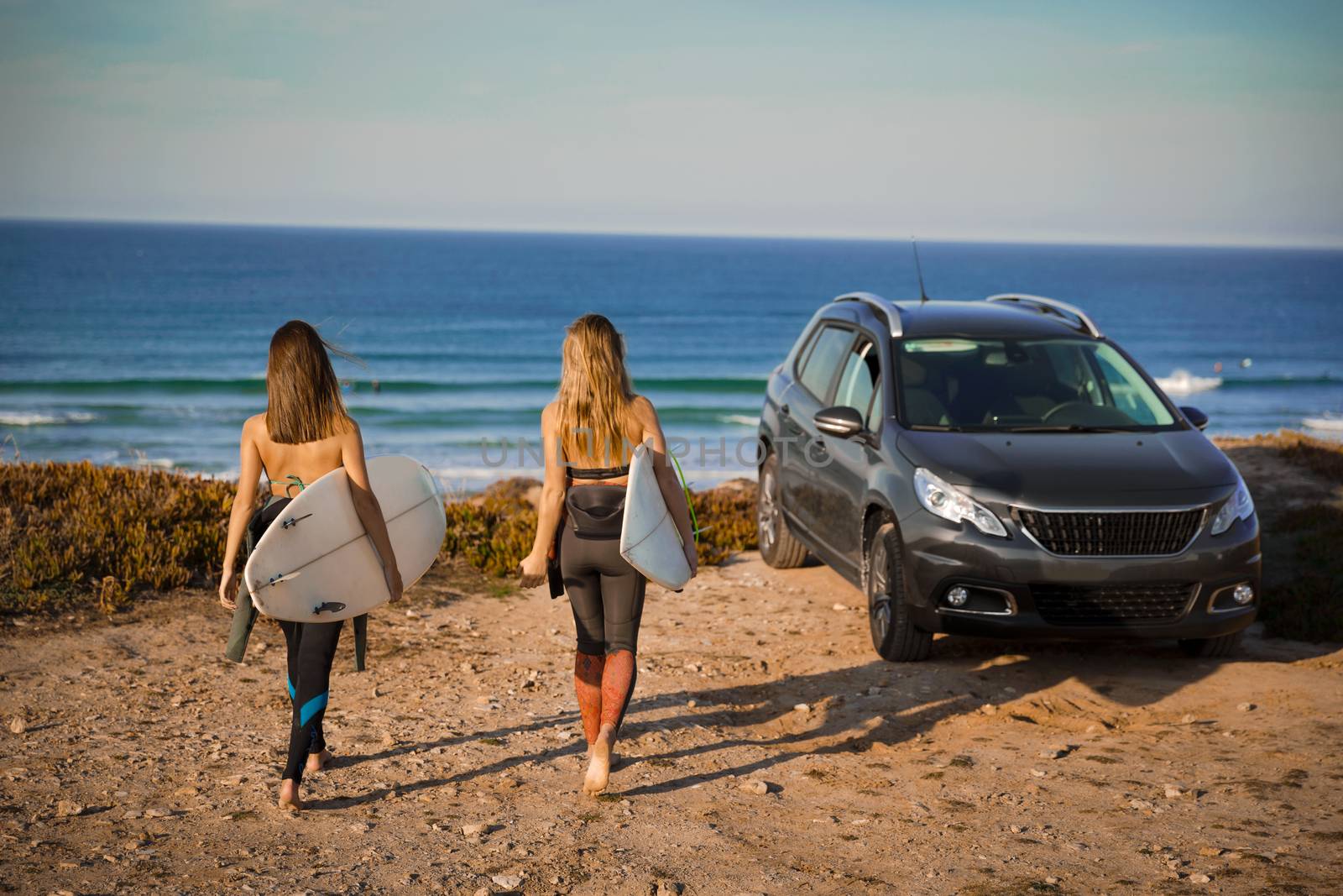 Two beautiful surfer girls near the coastline with her car, and getting ready for surfing