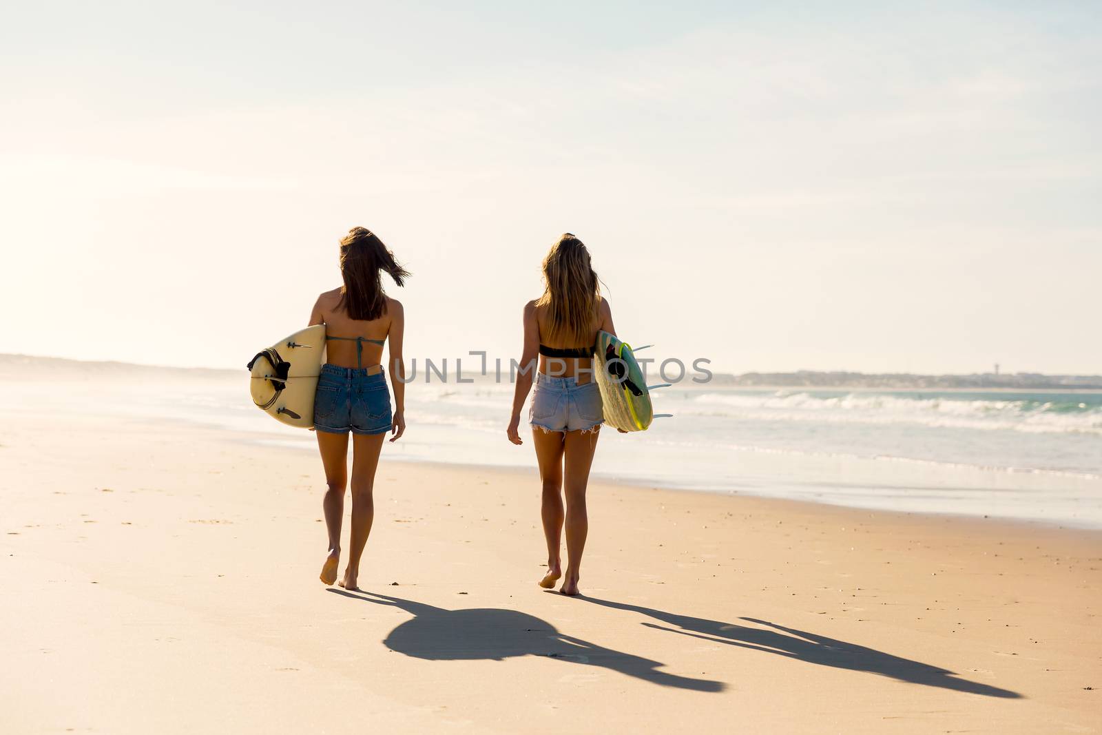 Surfer girls walking on the beach by Iko