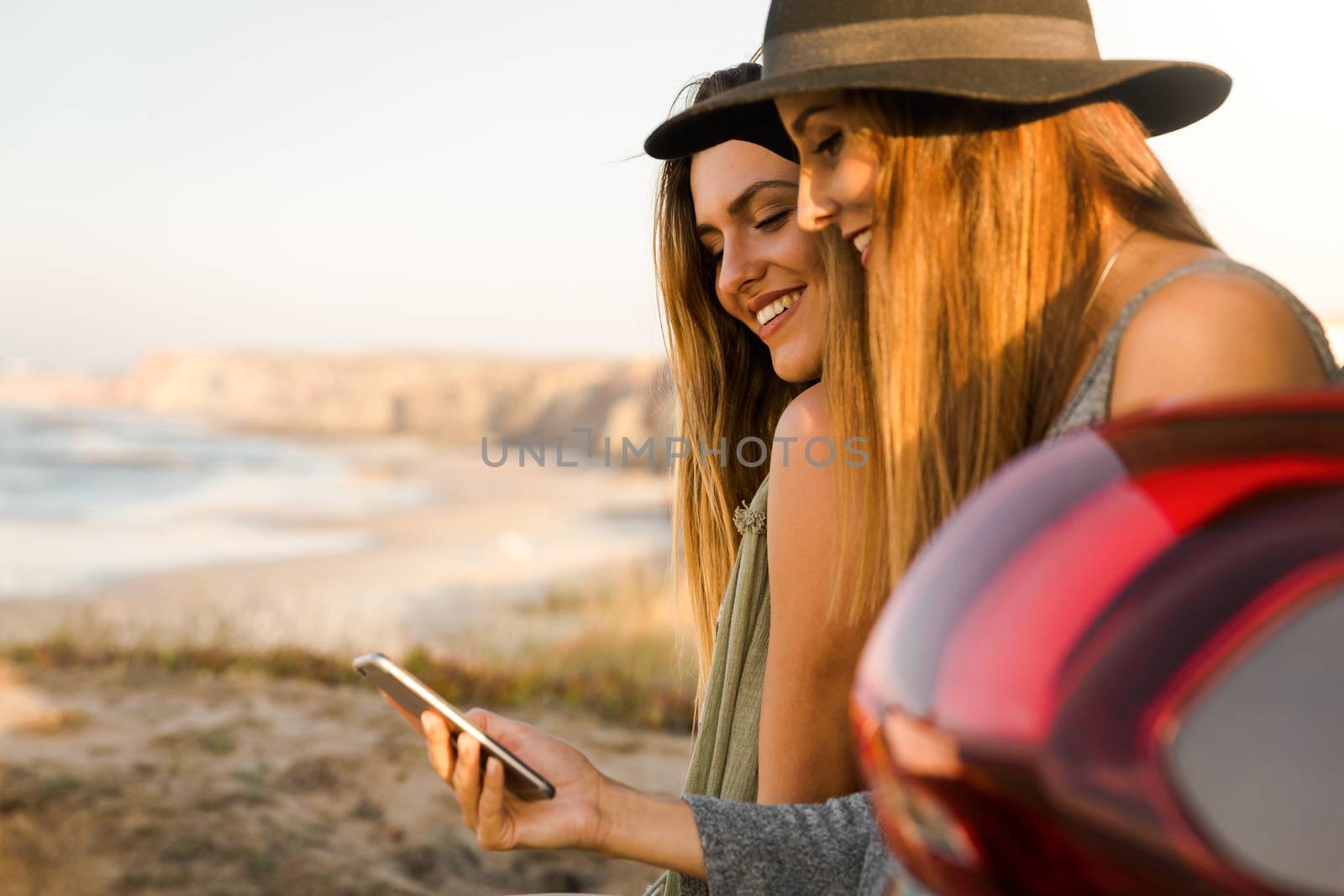 Two friends sitting in the trunk of a car while watching something on the phone