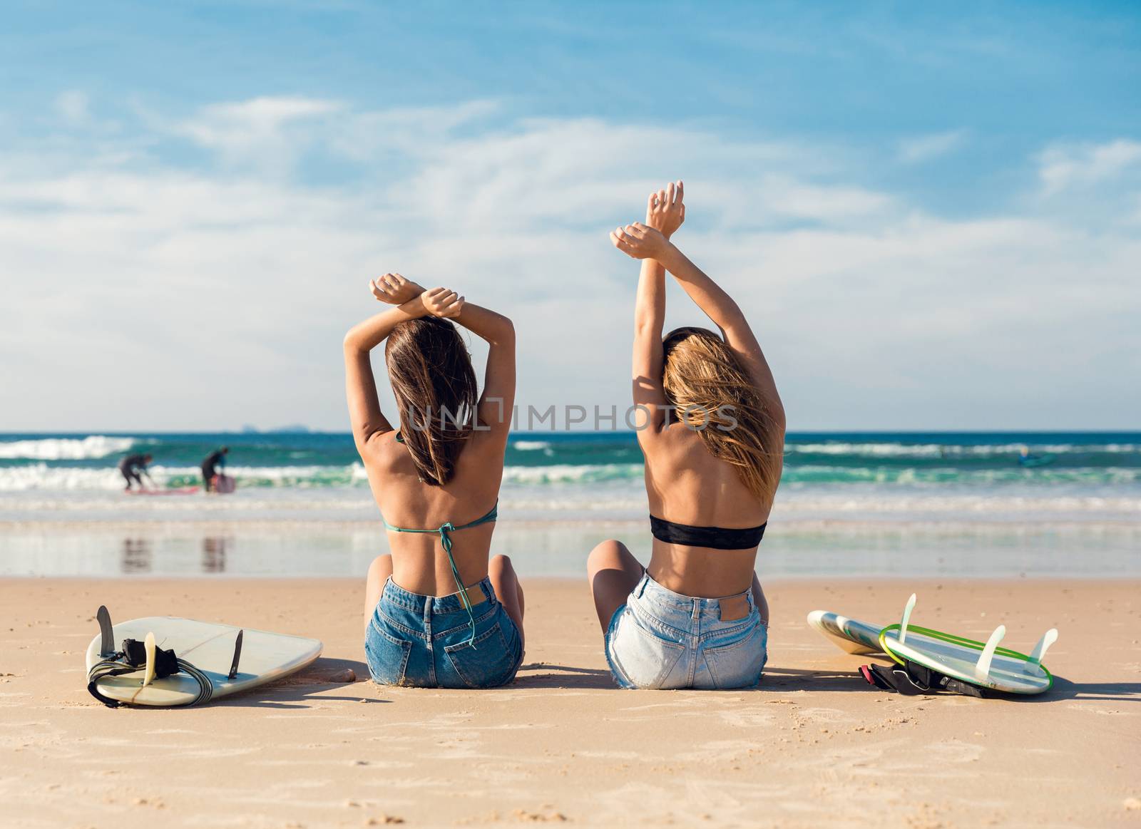 Two beautiful surfer girls at the beach with arms open