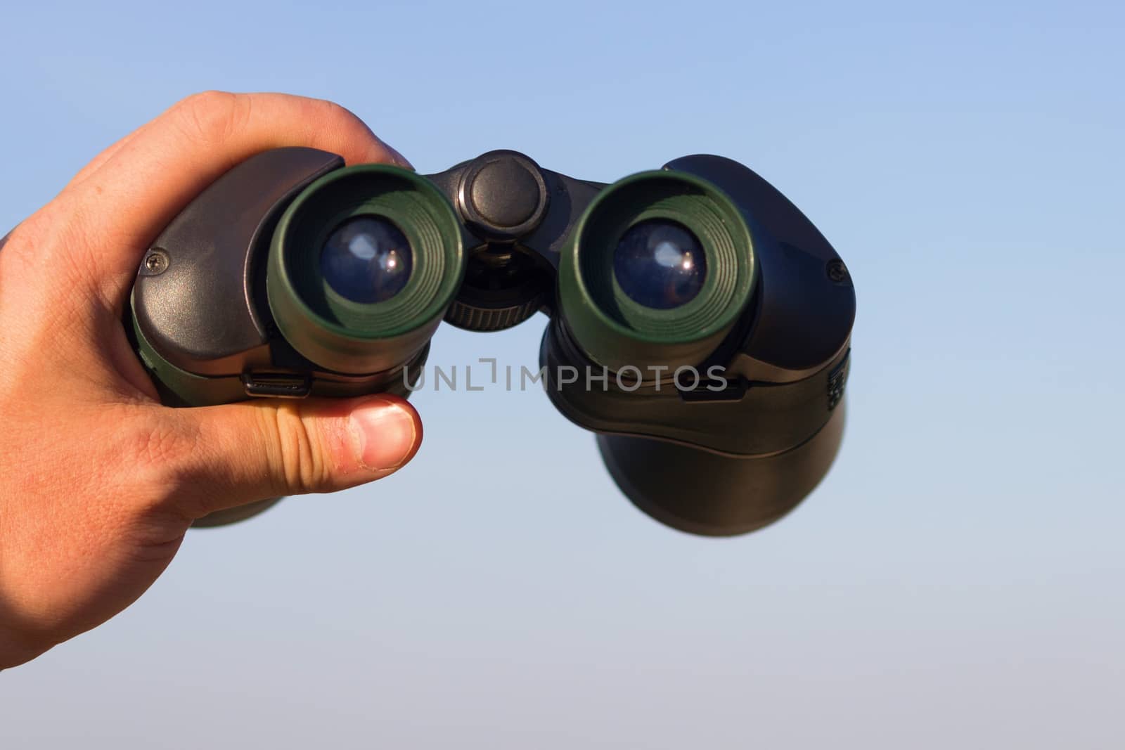 binocular in mans hands on the blue sky background