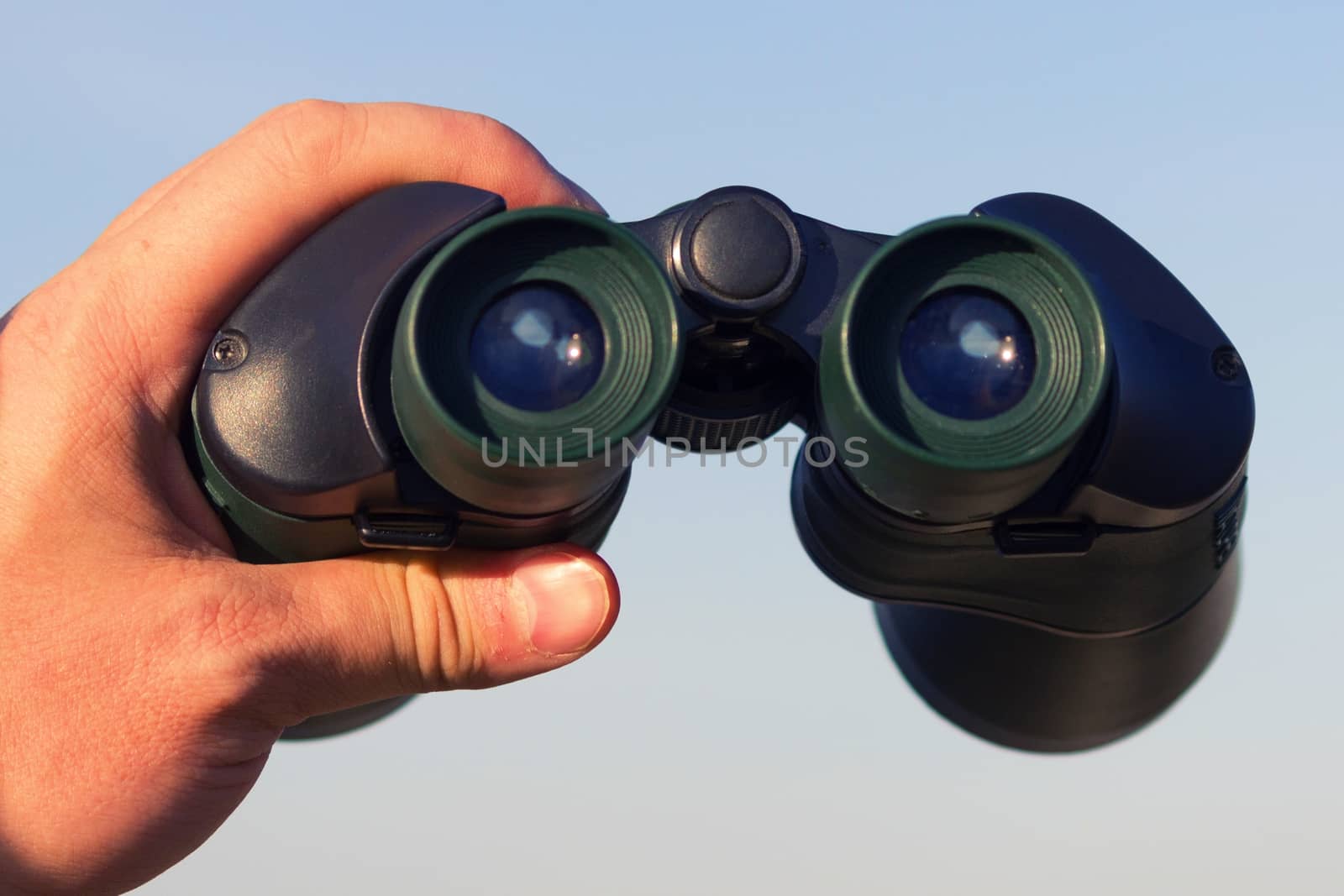 binocular in mans hands on the blue sky background