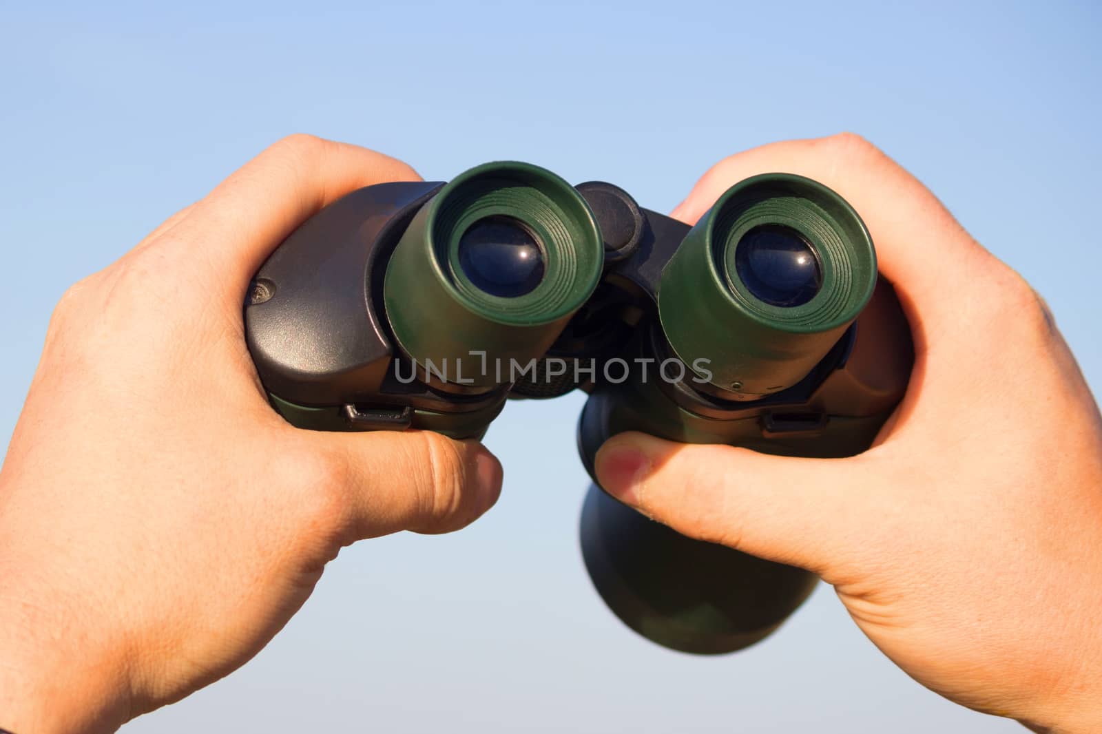 binocular in mans hands on the blue sky background