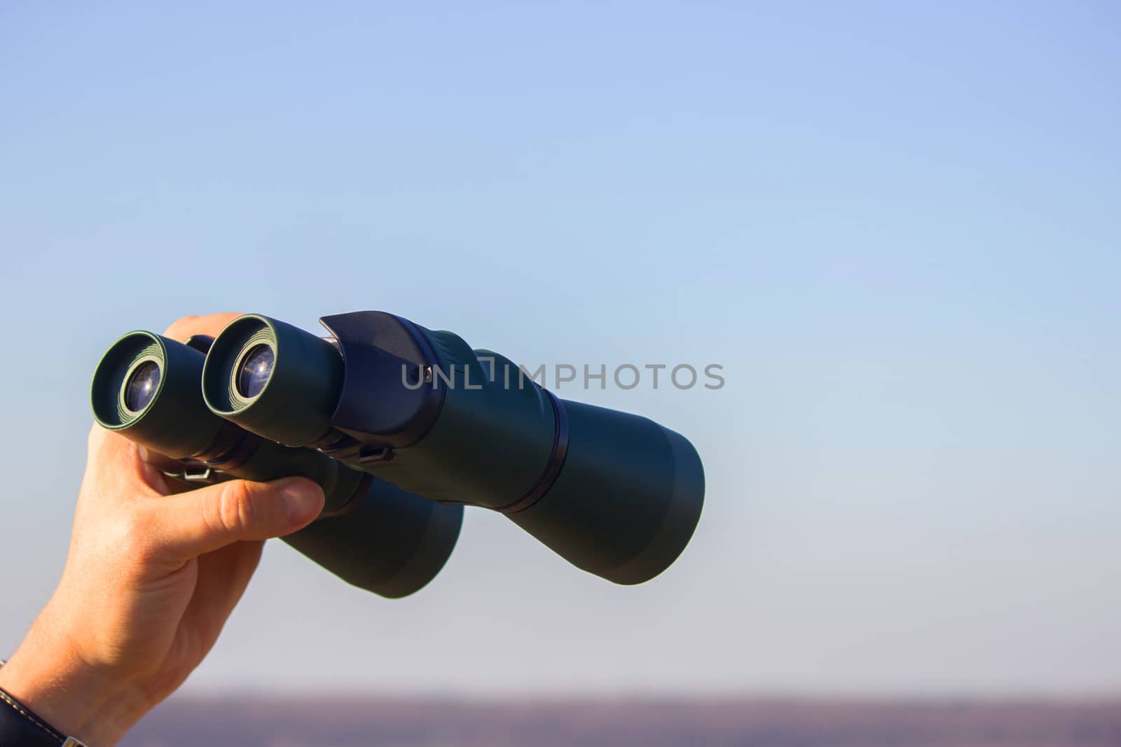 binocular in mans hands on the blue sky background