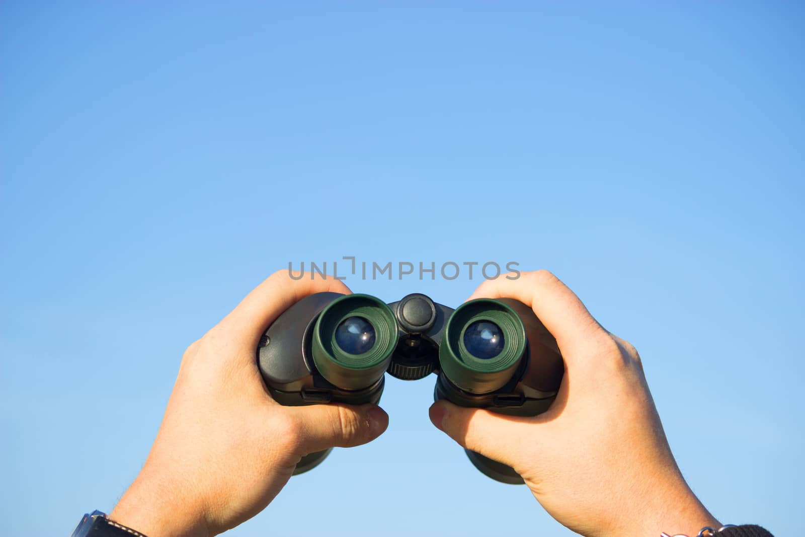 binocular in mans hands on the blue sky background