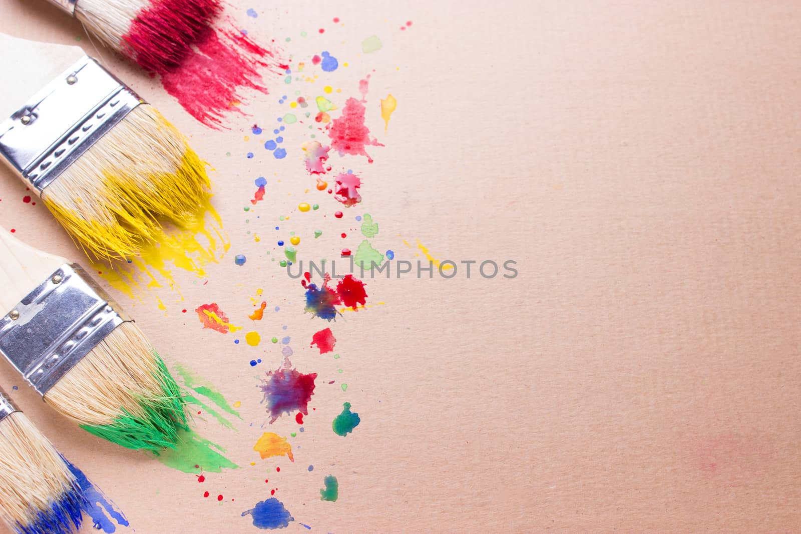 Different sizes paintbrushes against a background of multicolored paint spread. copy space