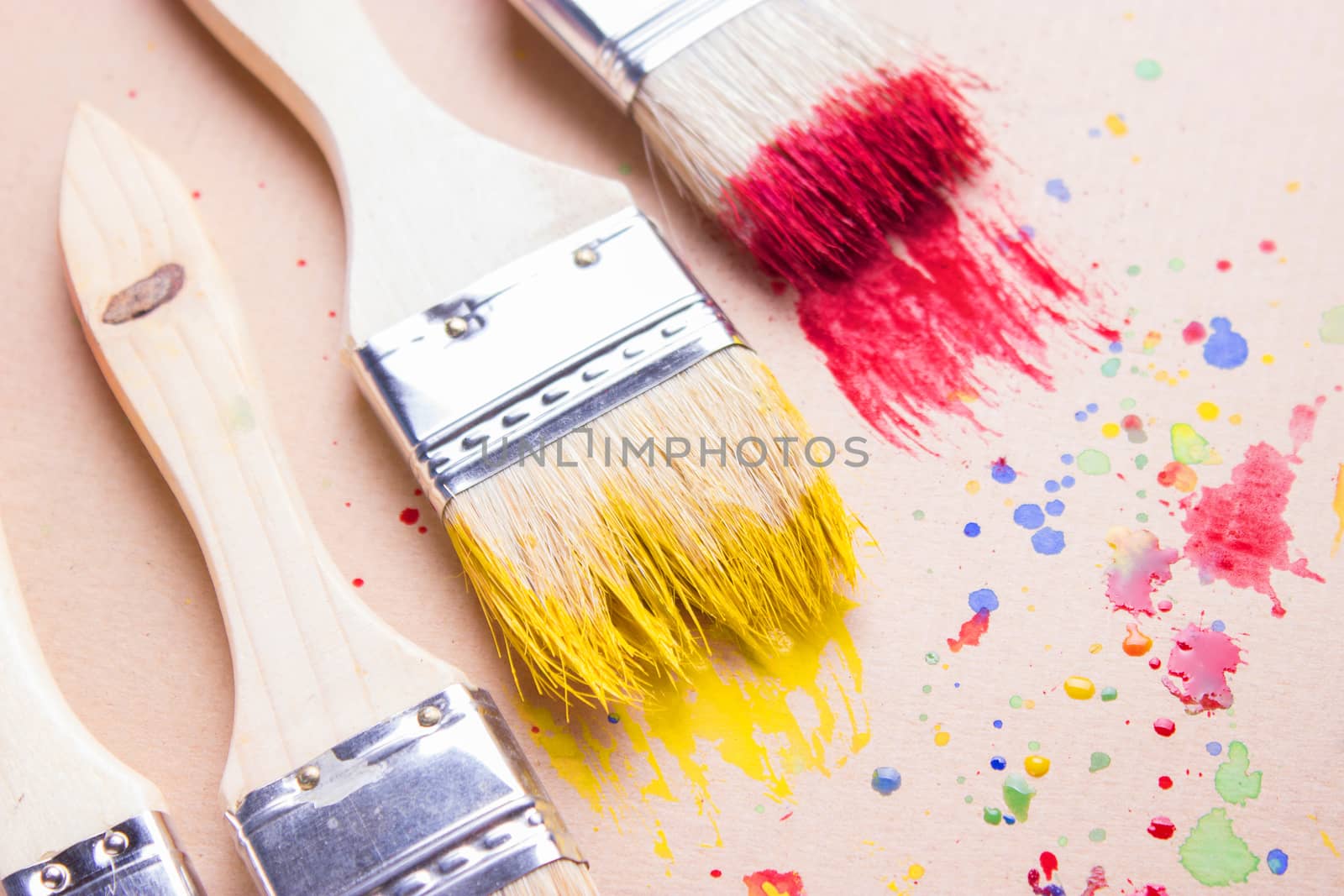 Different sizes paintbrushes against a background of multicolored paint spread.