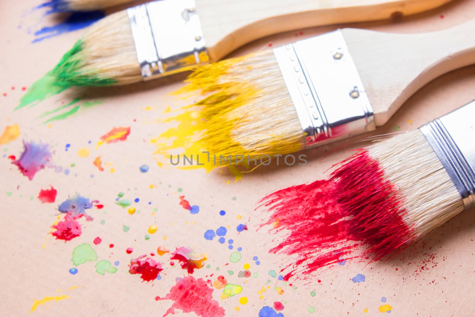 Different sizes paintbrushes against a background of multicolored paint spread.