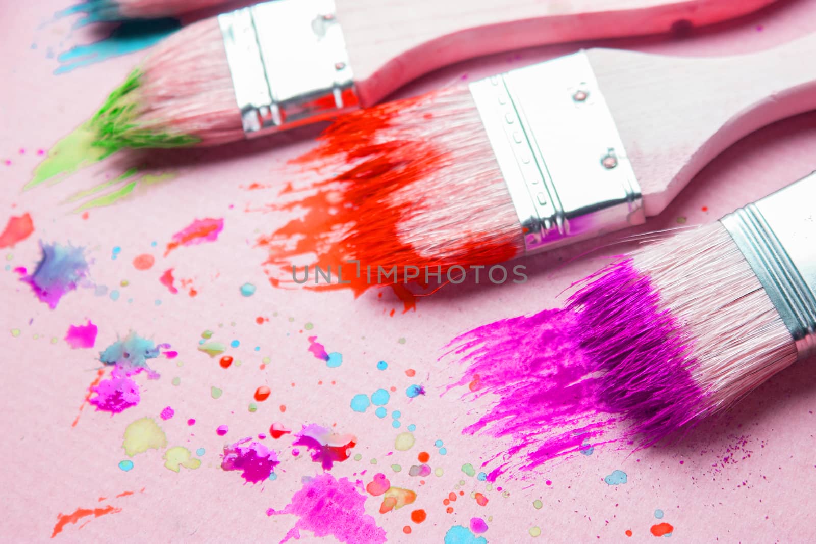 Different sizes paintbrushes against a background of multicolored paint spread.