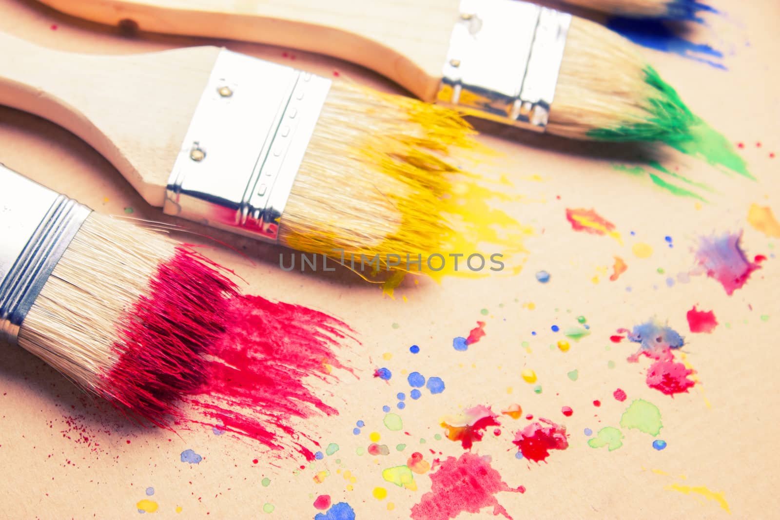 Different sizes paintbrushes against a background of multicolored paint spread.