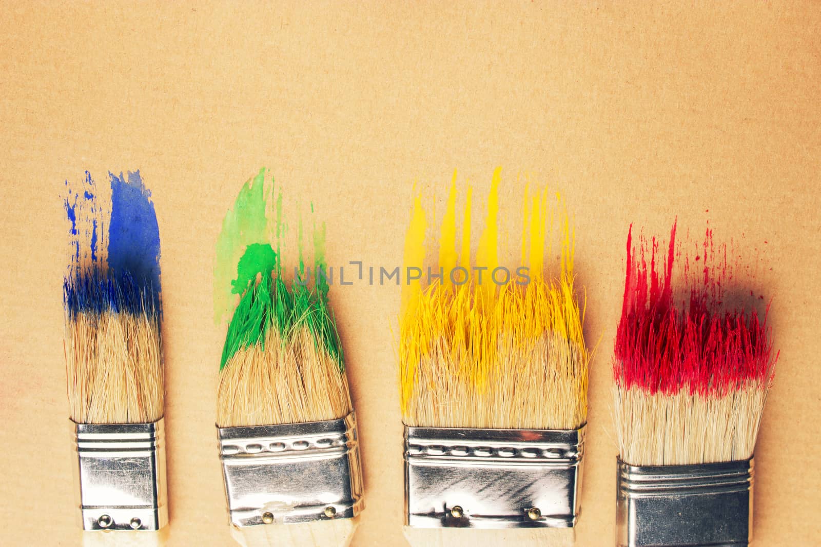 Different sizes paintbrushes against a background of multicolored paint spread.