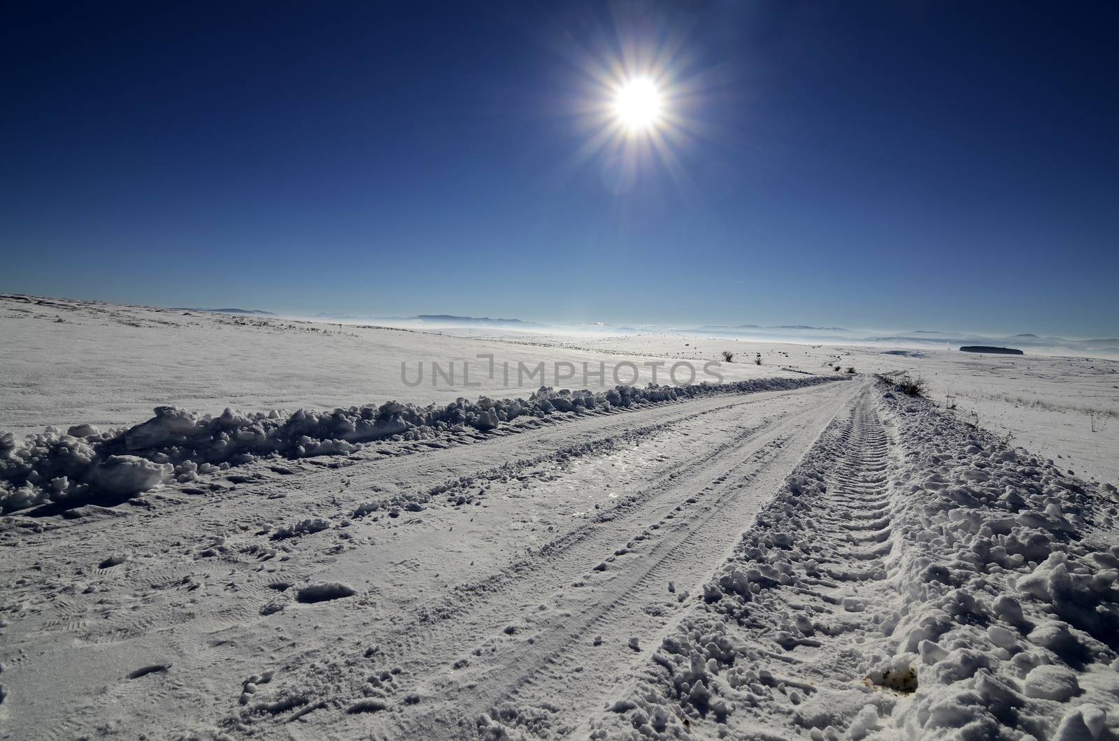 Landscape of road on the empty field covered with snow and ice on sunny day