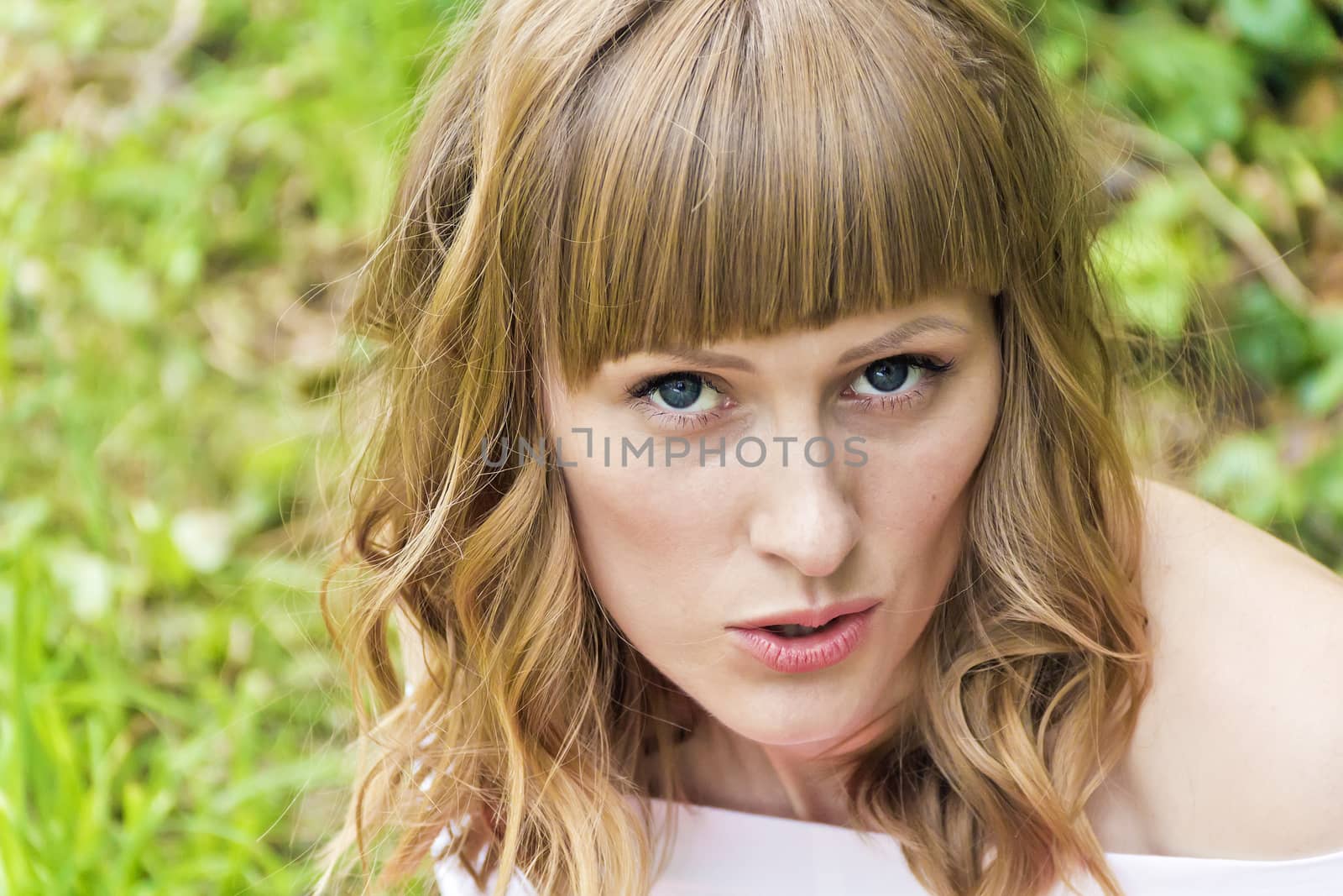 Horizontal portrait of young talking woman with big blue eyes on summer background