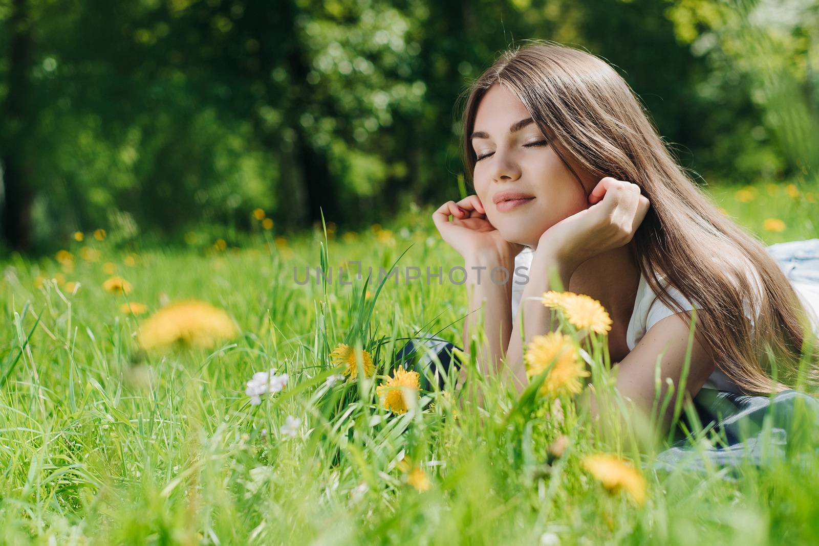 Beautiful young woman laying on grass with dandelion flowers in park