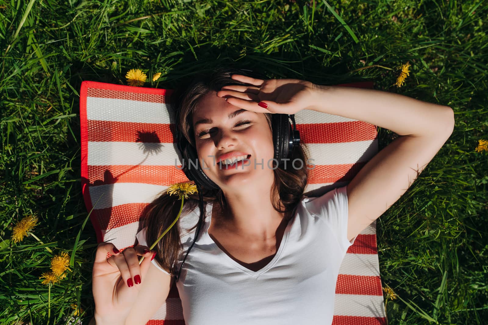 Young brunette woman with headphones listening to the music outdoors on sunny summer day