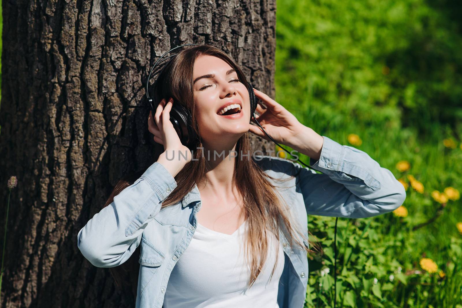 Young brunette woman with headphones listening to the music in park on sunny summer day