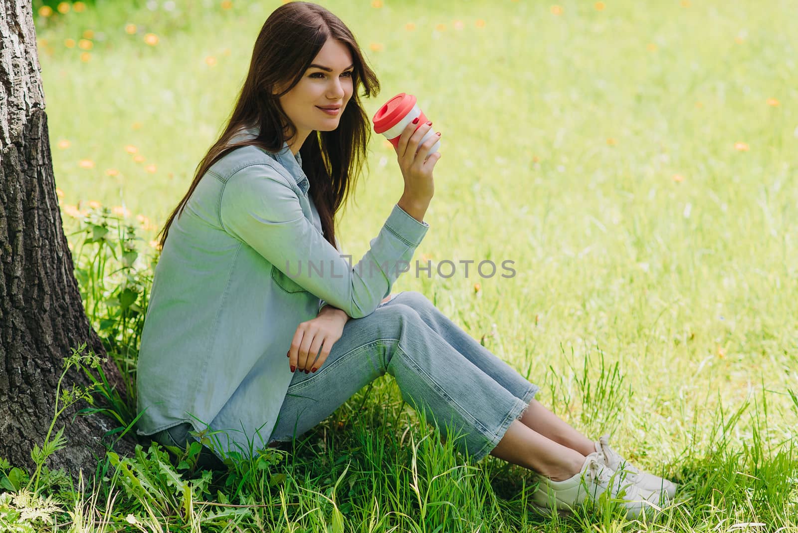 Beautiful girl enjoying a cup of coffee sitting under tree in park