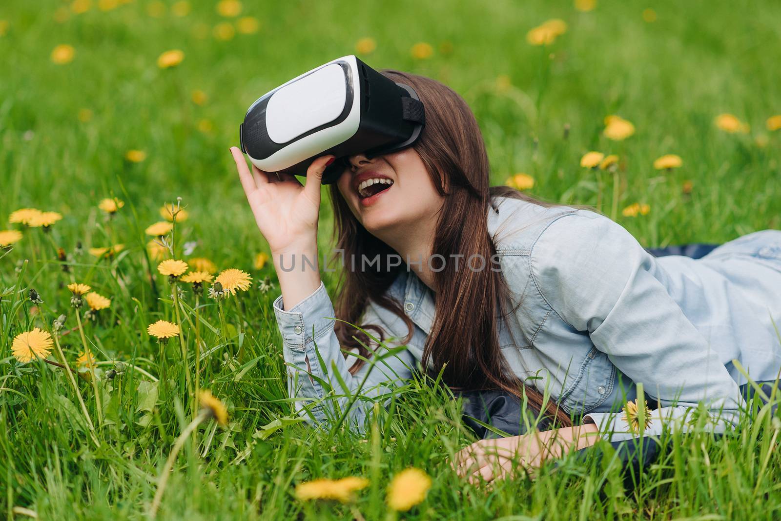 Woman using the virtual reality headset outdoors laying in spring flower field