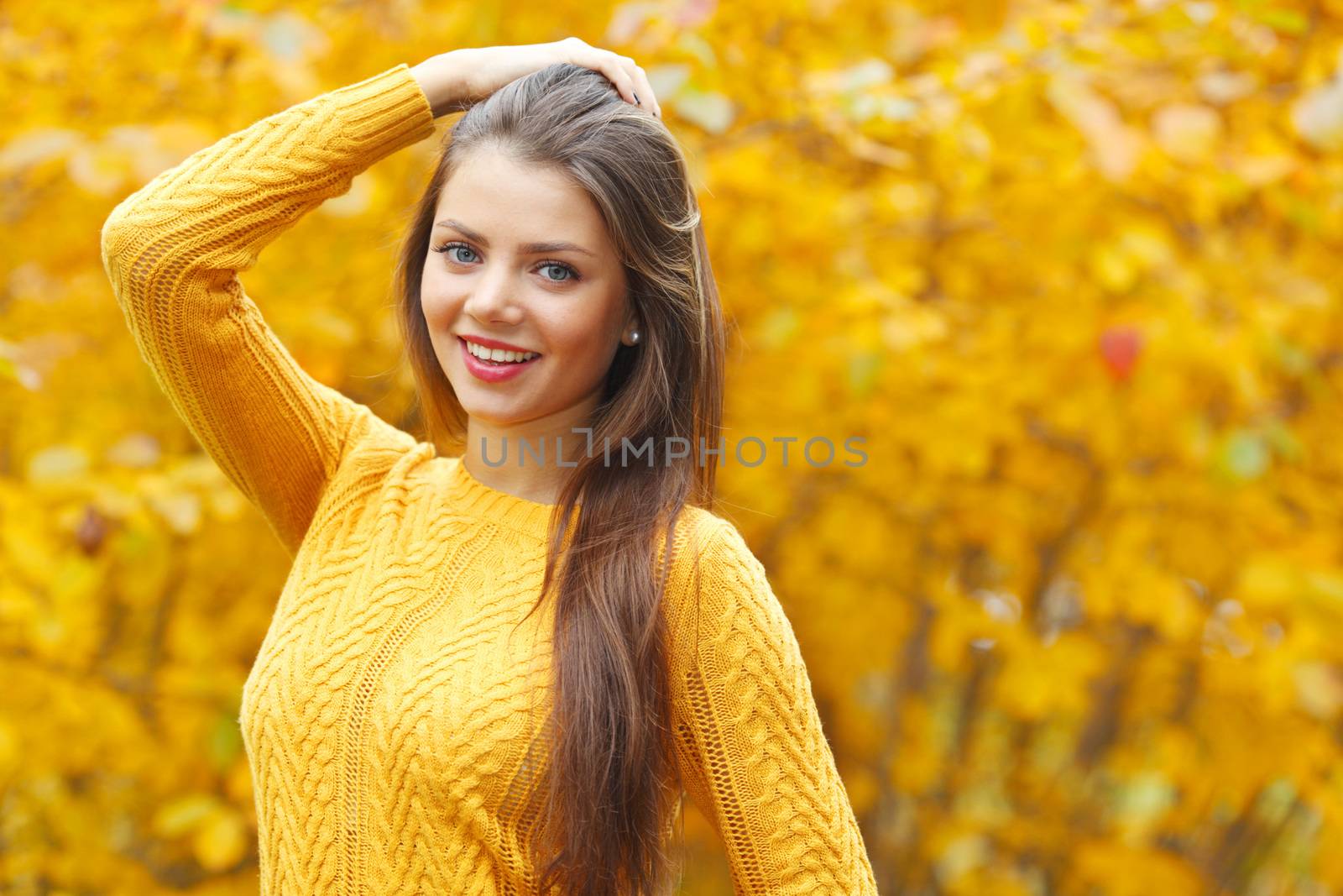 Young smiling brunette posing in autumn park on yellow trees background