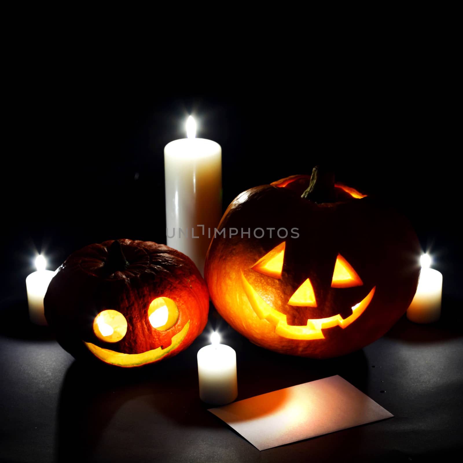 Halloween pumkins, candles and postcard on dark background