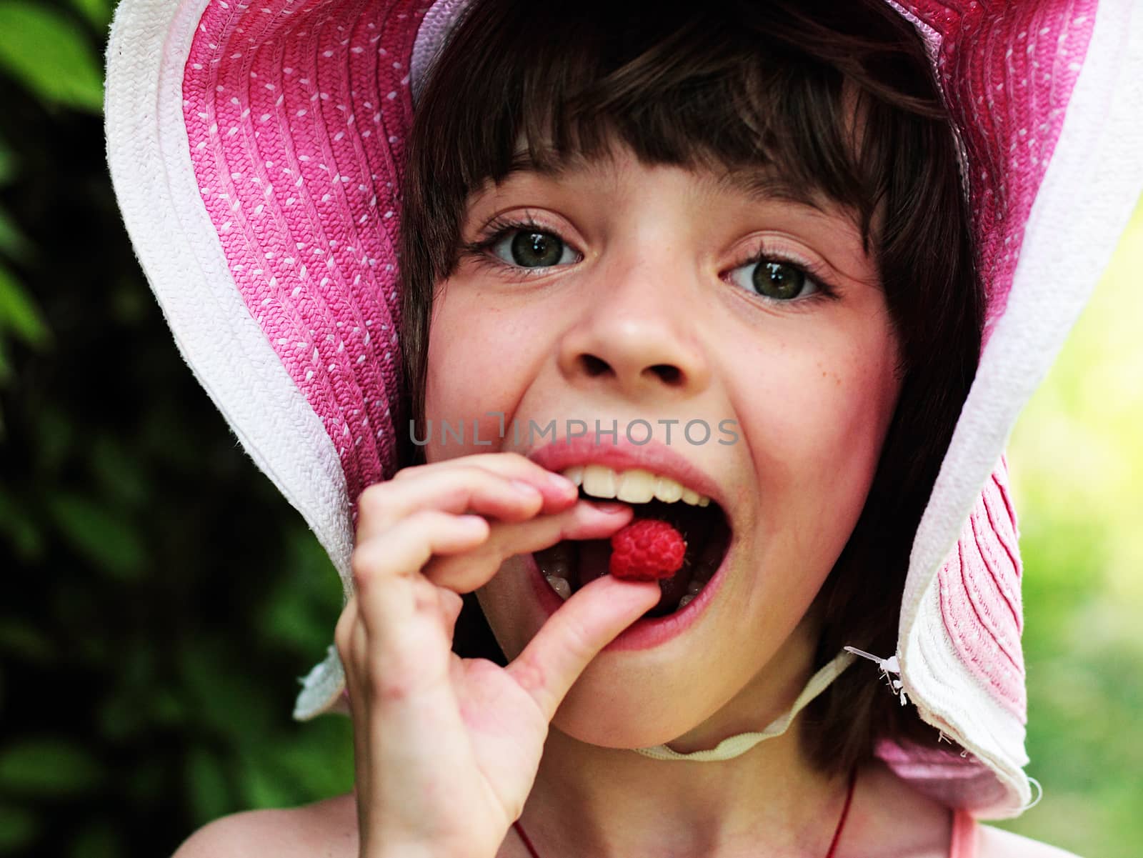 A girl in a hat is eating raspberries. by andsst