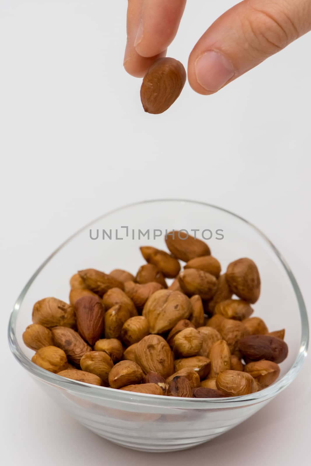 person droping pealed hazelnuts to the glass bowl