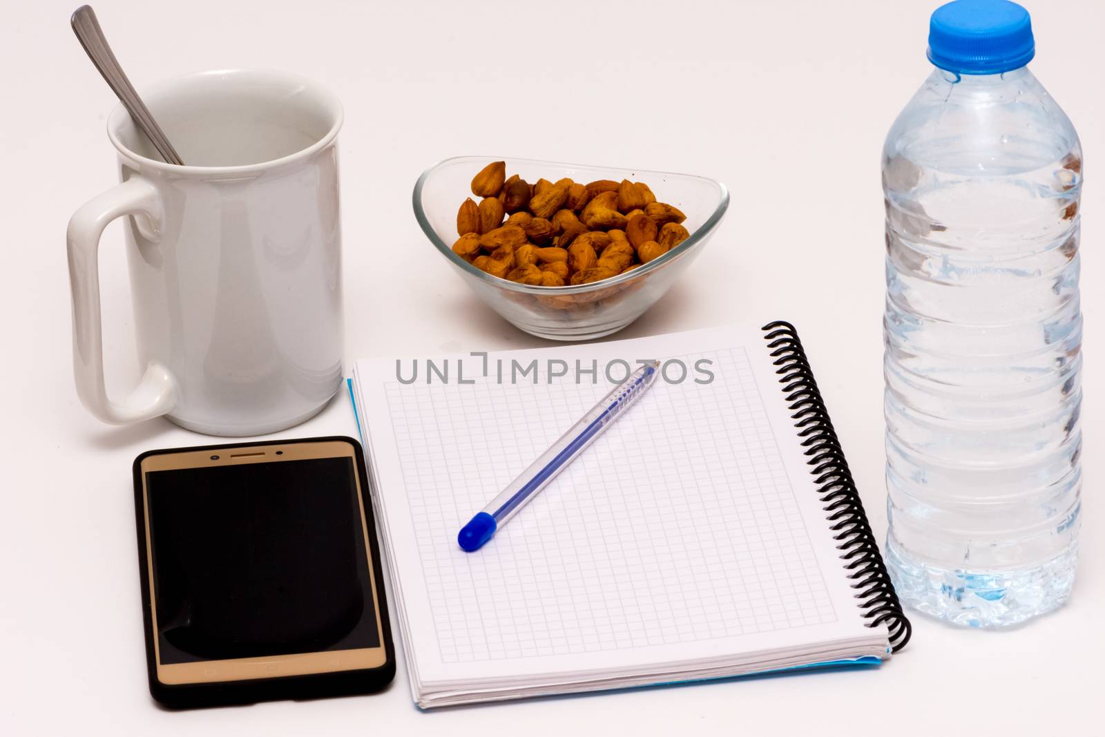 mobile phone and notebook on the desk with bowl of huzelnuts, bottle of water and the cup of coffee for keeping energy while working