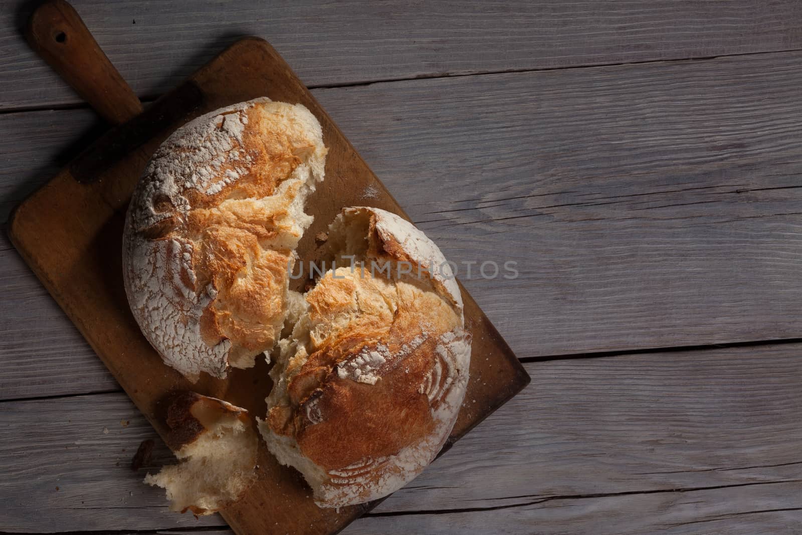 Torned crannied rustical homemade bread loaf on old cutting board over grey wooden table. Dark background with a free space.