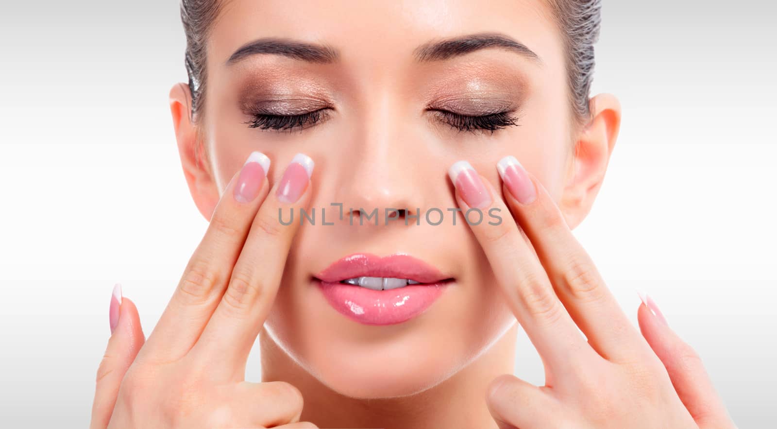 Pretty woman massaging her face against a grey background with copyspace